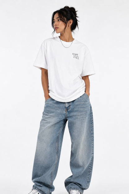 A model wearing a white short-sleeve t-shirt with a small black graphic on the left chest, paired with wide-leg light blue jeans, against a plain white studio background.