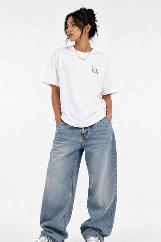 A model wearing a white short-sleeve t-shirt with a small black graphic on the left chest, paired with wide-leg light blue jeans, against a plain white studio background.
