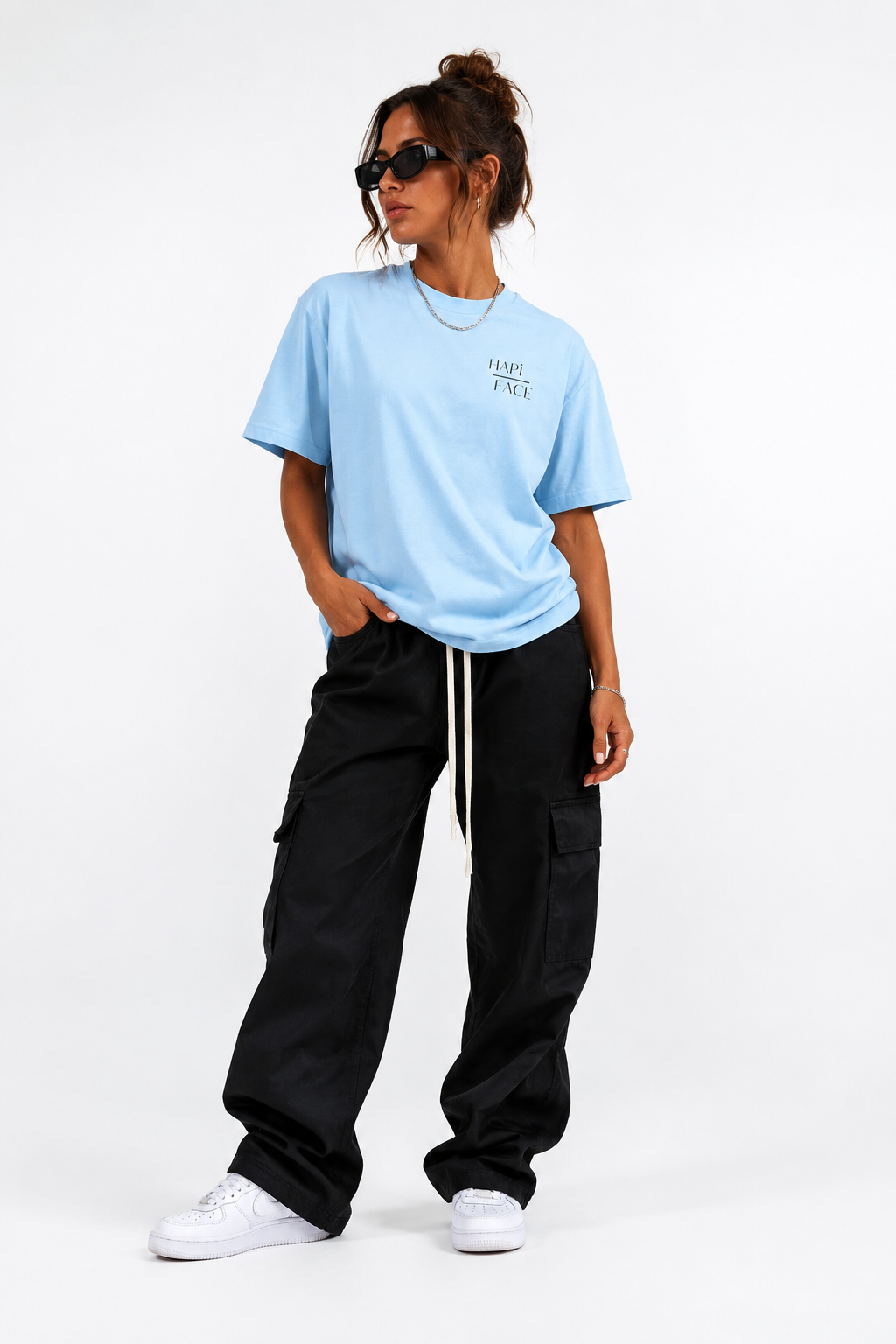 A woman modeling a light blue crewneck t-shirt with 'FLIP FAFT' printed on the chest, paired with black cargo pants and white sneakers, against a plain white studio background.